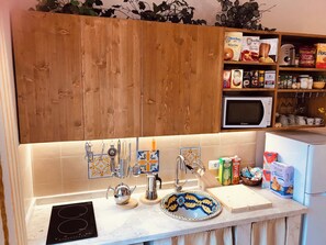 Eine Küche mit Holzausstattung, einer Mikrowelle, einem Spülbecken mit hängendem Besteck und verschiedenen Lebensmitteln auf der Arbeitsfläche.