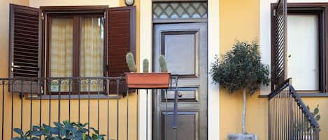 Un edificio residencial con fachada amarilla, una puerta con panel de vidrio y una pequeña planta en maceta en el porche.
