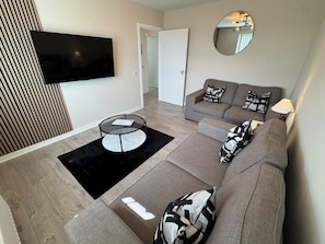 A modern living room with a sofa, a coffee table, and a flat-screen TV mounted on the wall.