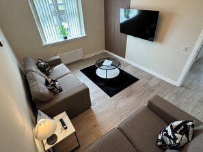 A modern living room with a sectional sofa, a coffee table, and a flat-screen TV mounted on the wall.
