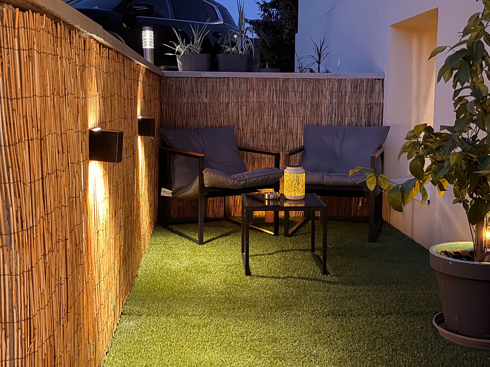 Un área de estar al aire libre con pared de bambú, un sofá y una mesa con un farol.