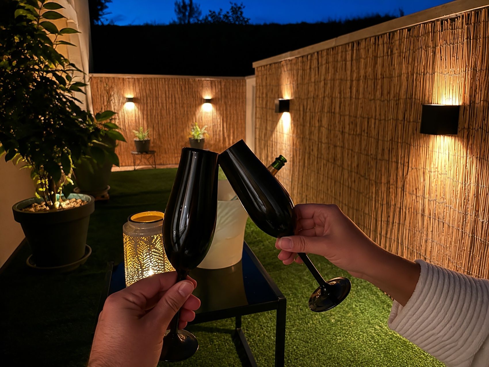 Deux personnes tenant des verres à vin, une table avec une bougie et un mur en bambou agrémenté de lampes murales.