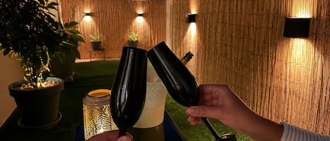 Två personer som håller vinglas, ett bord med ett ljus och en vägg av bambu med väggmonterade lampor.