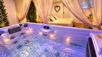 A spa room with a hot tub, a bed, and a heart-shaped wall decoration.