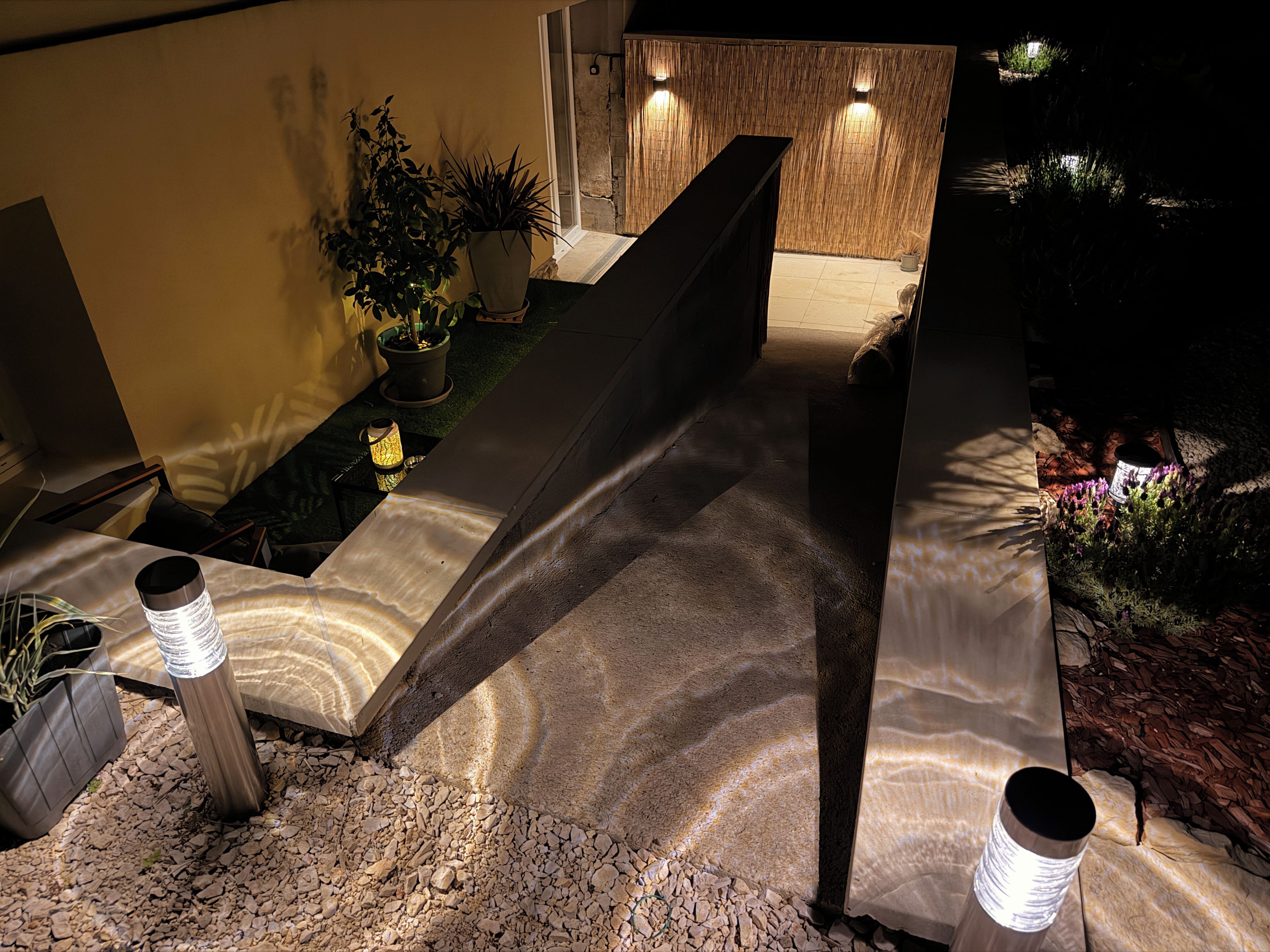 Un espace extérieur moderne agrémenté d’un banc en pierre, de plantes en pot et d’une structure en bois.