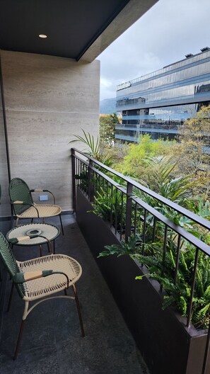 A balcony with wicker furniture, a concrete wall, and a view of a modern building and greenery. - Nostos Bogotá Hotel (Bogotá)