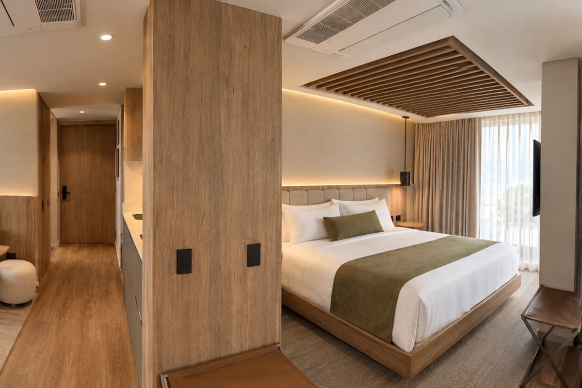 Una habitación de hotel con sofá, cama, una mesita y televisor montado en la pared.