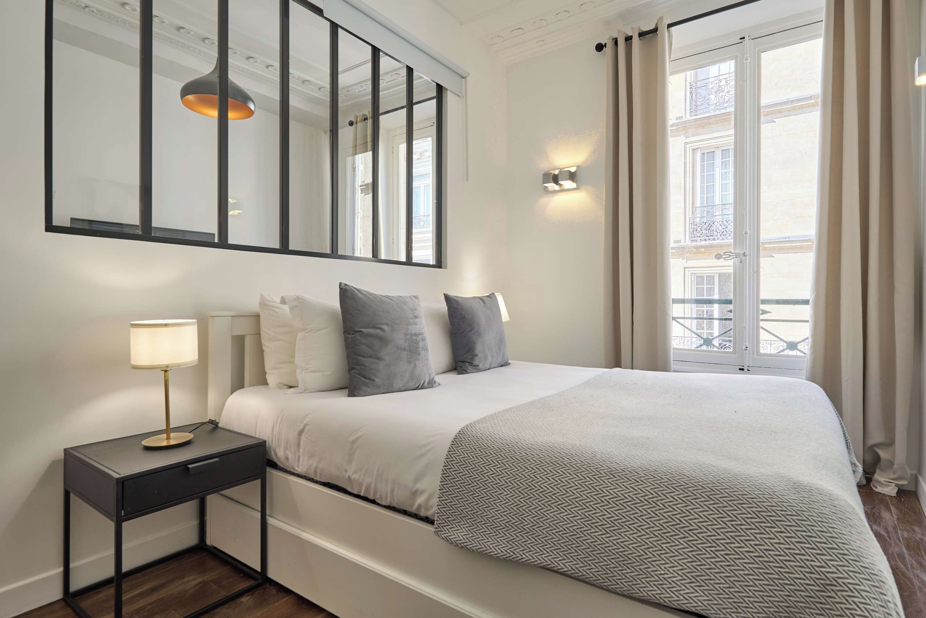 Une chambre d’hôtel avec un grand lit, une table de chevet avec une lampe, un miroir et une vue sur la ville par la fenêtre.