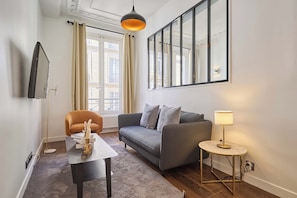 A modern living room with a sofa, a coffee table, a lamp, and a TV mounted on the wall. - Charming Apartment Montaigne Champs Elysees (Paris)
