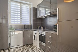 A compact kitchen with a washing machine, a built-in oven, and a coffee maker. - Charming Apartment Montaigne Champs Elysees (Paris)