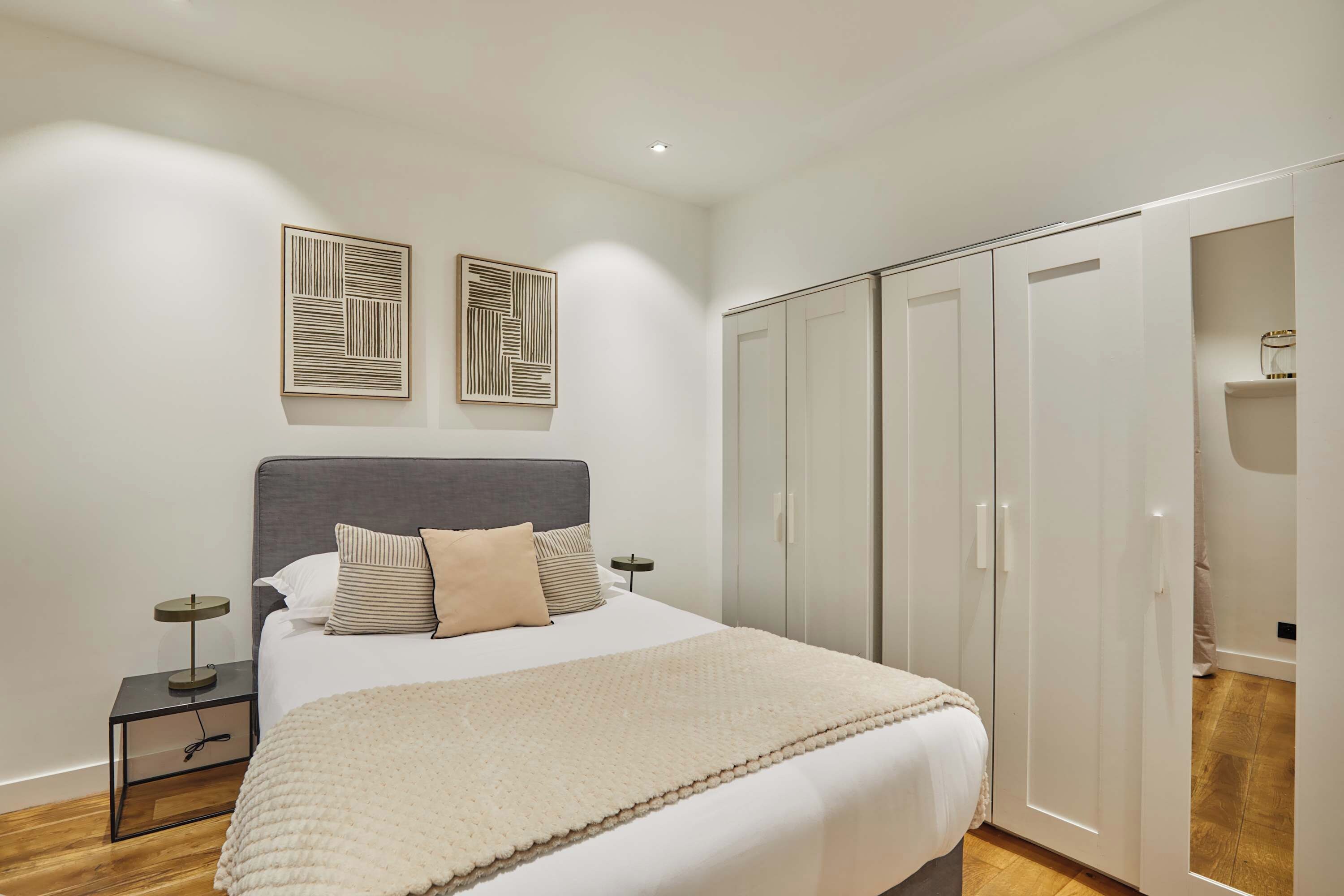 A bedroom with a bed, bedside tables, a wardrobe, and two wall art pieces.