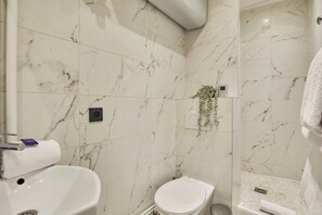 Ein Badezimmer mit weißem Marmorboden, einem weißen Waschbecken, einer Toilette und einer Duschkabine.