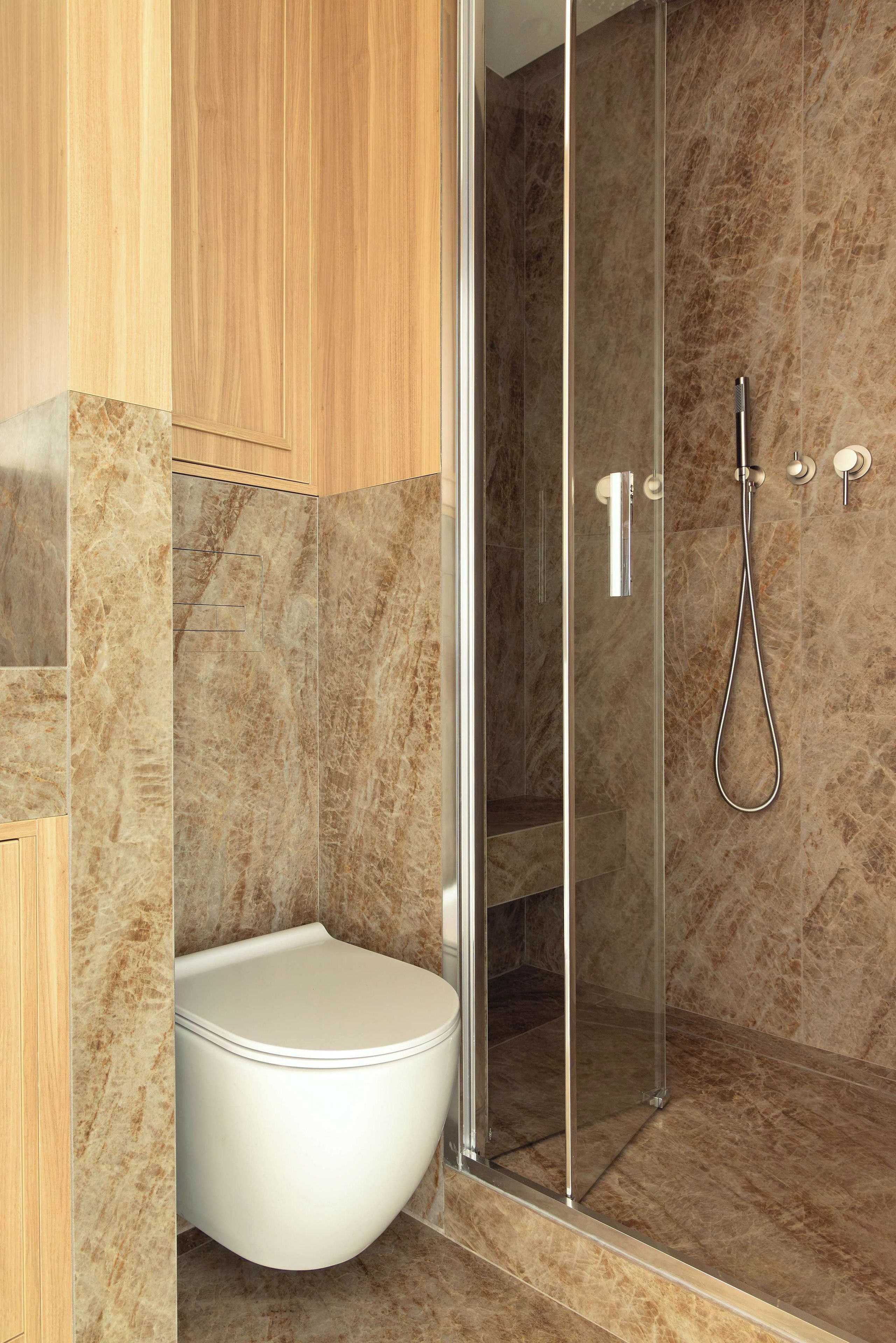 Ein modernes Badezimmer mit einer gläsernen Duschkabine, Toilette und Marmorboden.