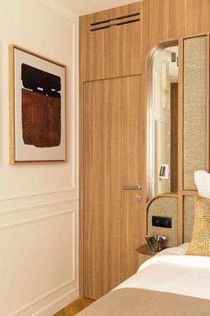 A hotel room with a wooden wardrobe, a bed with a patterned pillow, a framed artwork on the wall, and a mirror reflecting part of the room. - Sublime Suite Saint Honoré, Elysée Palace (Paris)