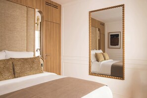 A hotel room with a bed, a wooden wardrobe, a large mirror, and a framed artwork on the wall. - Sublime Suite Saint Honoré, Elysée Palace (Paris)