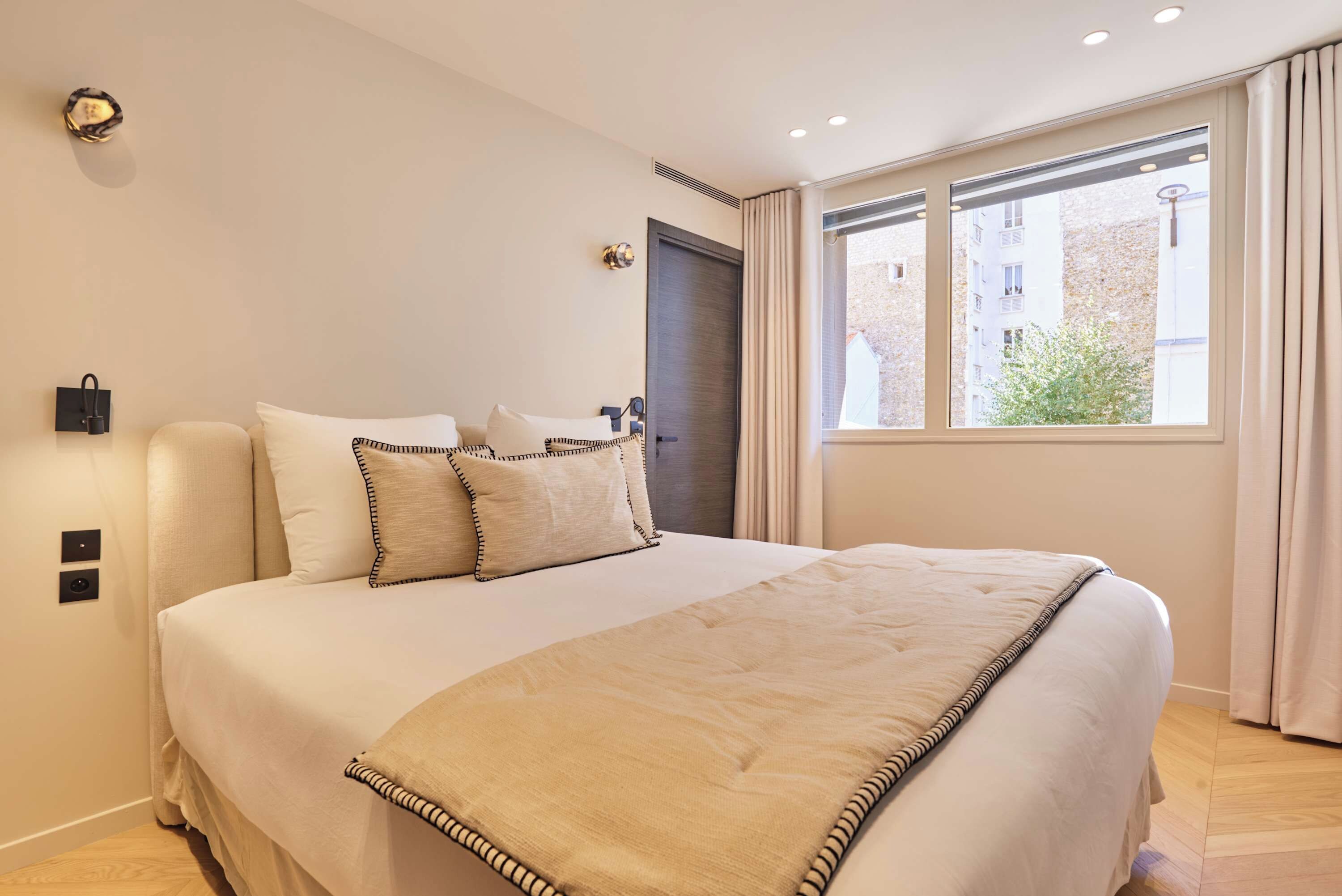Ein Hotelzimmer mit einem Bett, einem Fenster mit Vorhängen, einer Tür und einer Wandleuchte.