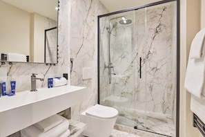Un bany modern amb plat de dutxa de marbre, un lavabo blanc i un vàter.