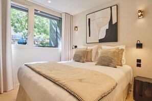 A bedroom with a large bed, a window with curtains, a painting on the wall, and a small table. - Sublim Apartment AC St Germain Luxembourg Park (Paris)