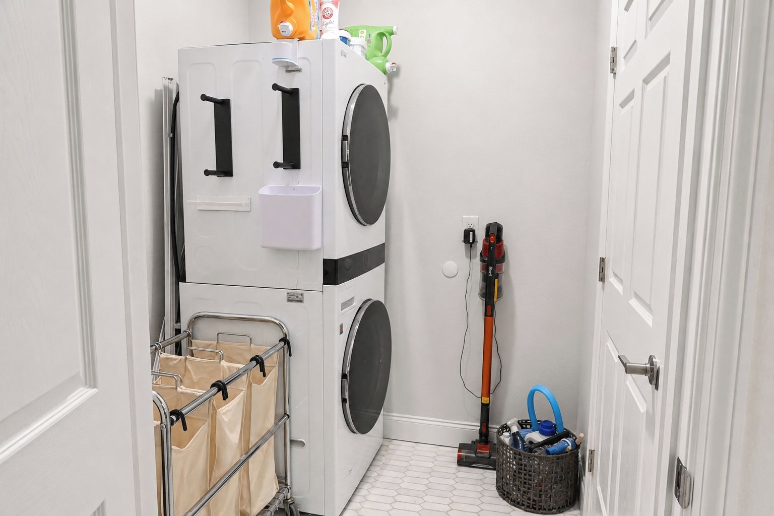 A laundry room with stacked washing machines, a cart with bags, and a vacuum cleaner.