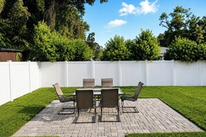 An outdoor patio with a brick table and chairs, surrounded by a white fence and lush greenery. - Your Tampa Home Away From Home. 3BR/2BA (Tampa)