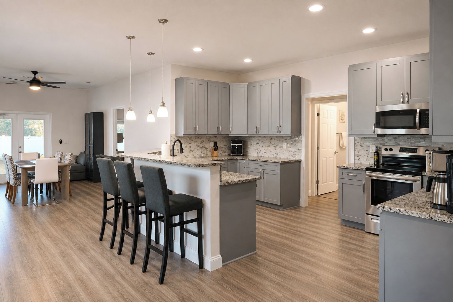 A modern kitchen with grey cabinets, a central island with bar stools, and stainless steel appliances.