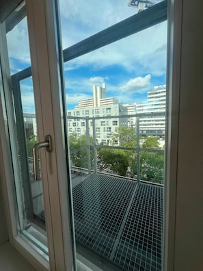 A window with a metal grid, overlooking a cityscape with multiple buildings and a clear sky.