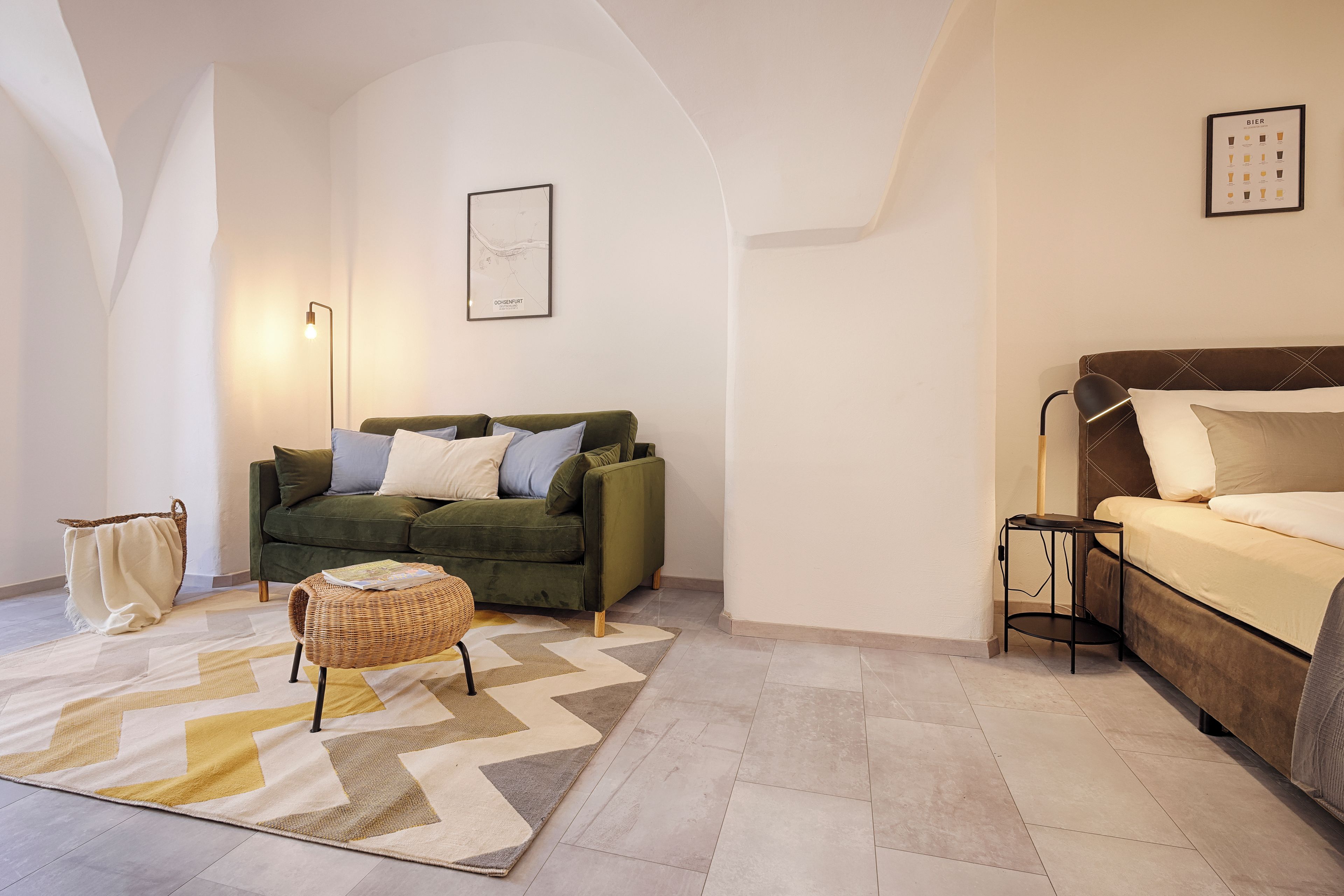 A cozy living room with a green sofa, a small round table, and a bed with a headboard.