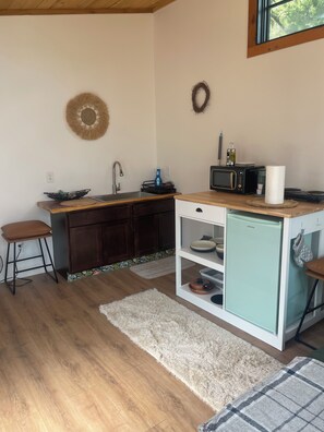 Cocina compacta con pileta, microondas y heladera pequeña. Hay taburetes y un alfombra en el piso.