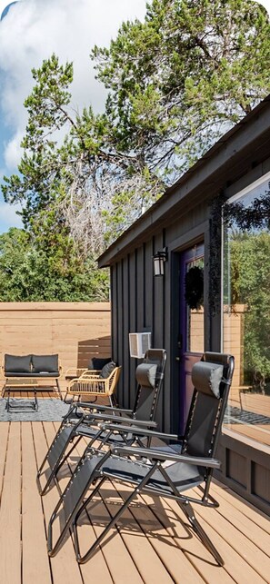 A deck with outdoor furniture, a building with a dark door, and a tree in the background. - Whimsical cabin near breweries and trails in charming Dripping Springs (Dripping Springs)