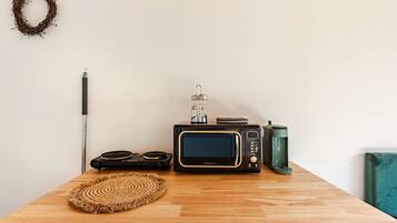 A wooden table with a woven placemat, a black microwave, a green mug, and a black speaker.