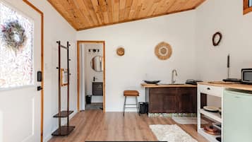 A compact kitchen with wooden flooring, a sink, a small stool, and a microwave.