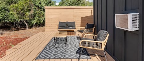 An outdoor patio with a wooden deck, a sofa, two chairs, and a patterned rug.
