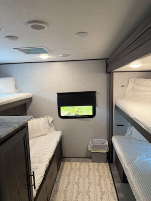 A compact RV interior with two bunk beds, a small window with a view, and a built-in sink. - Adventure Awaits! Come Camp, Glamp, and RV with us! Golf cart included! (Corbin)