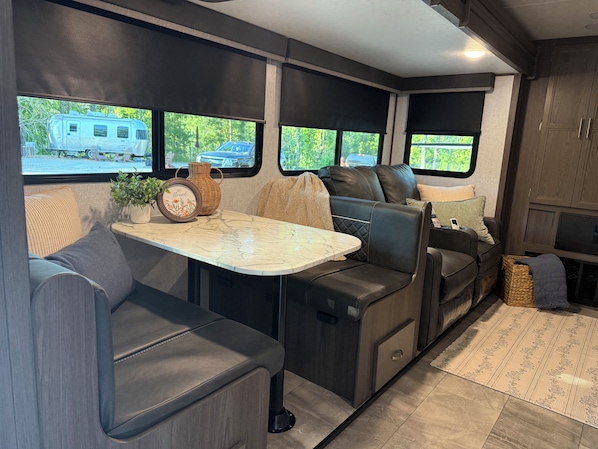 A compact RV interior with a dining area, seating, and a view of the outside. - Adventure Awaits! Come Camp, Glamp, and RV with us! Golf cart included! (Corbin)