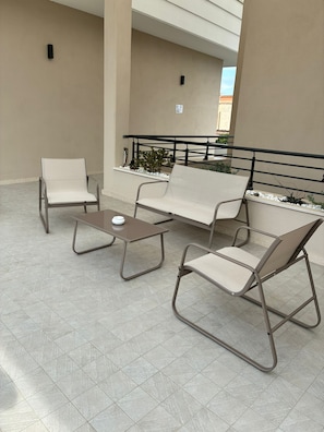 Un área de estar al aire libre con una mesa, dos sillas, un banco y una barandilla.