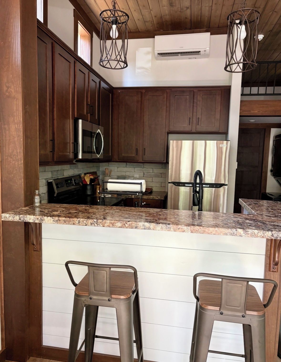 Una cocina con armarios de madera, electrodomésticos de acero inoxidable, encimeras de granito y dos taburetes de bar.