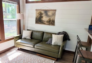A room with a green sofa, a hanging landscape painting, and a window with a view of greenery. - Peaceful mountain retreat at Selah (Mentone)
