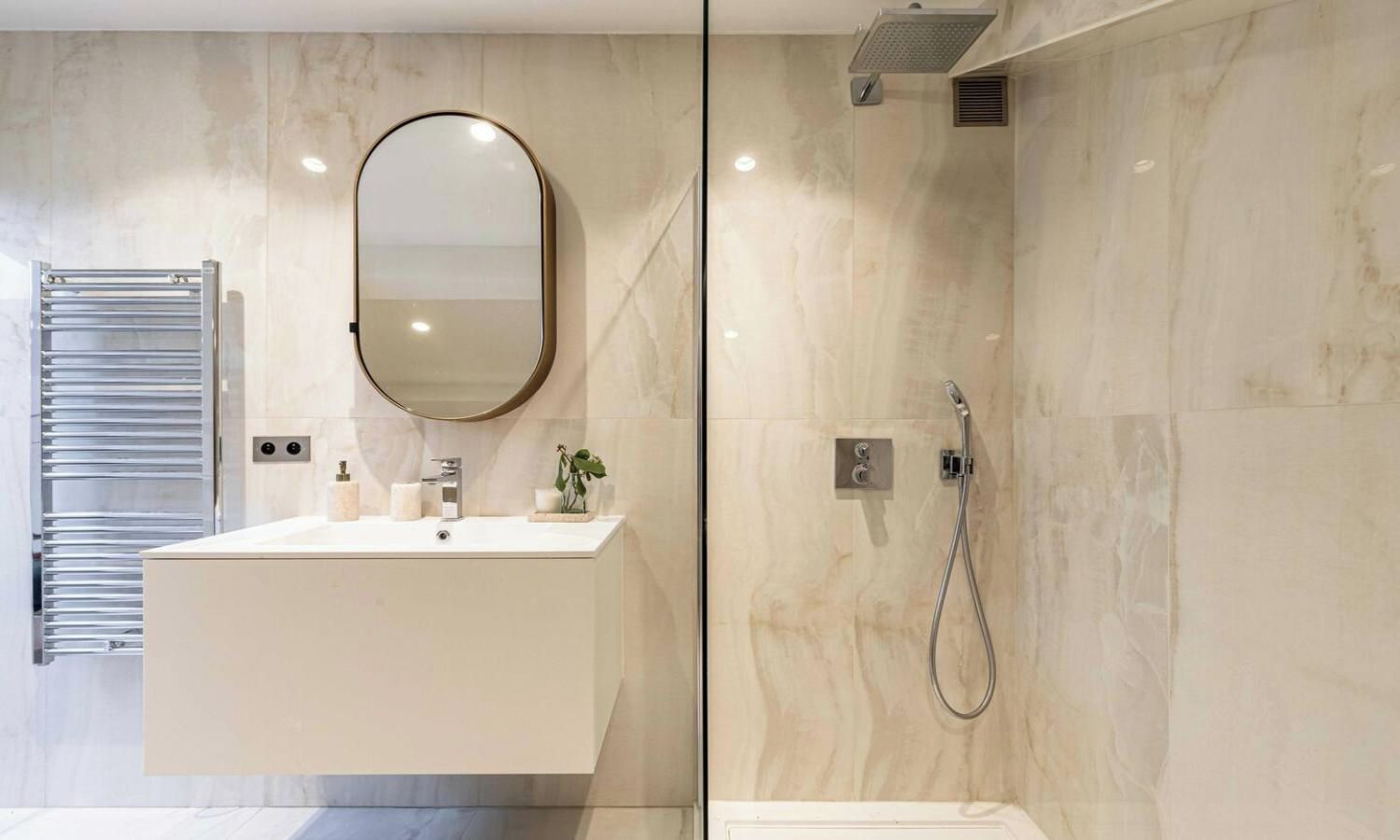 A modern bathroom with a glass-enclosed shower, a vanity with a mirror, and a towel rack.