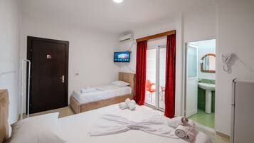 A hotel room with two beds, a TV, a sliding glass door to a balcony, and a bathroom with a sink and mirror.