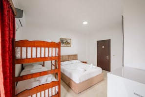 A hotel room with a bunk bed, a single bed, a desk, and a door.