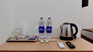 Habitación de hotel con una mesa de madera, dos botellas de agua, una tetera, una bandeja con vasos y pañuelos de papel, un control remoto y un pequeño dispositivo electrónico.