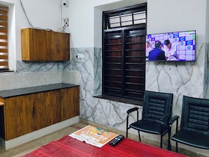 Una habitación con un armario de madera, una pared de mármol, un televisor mostrando un evento deportivo y una alfombra roja.