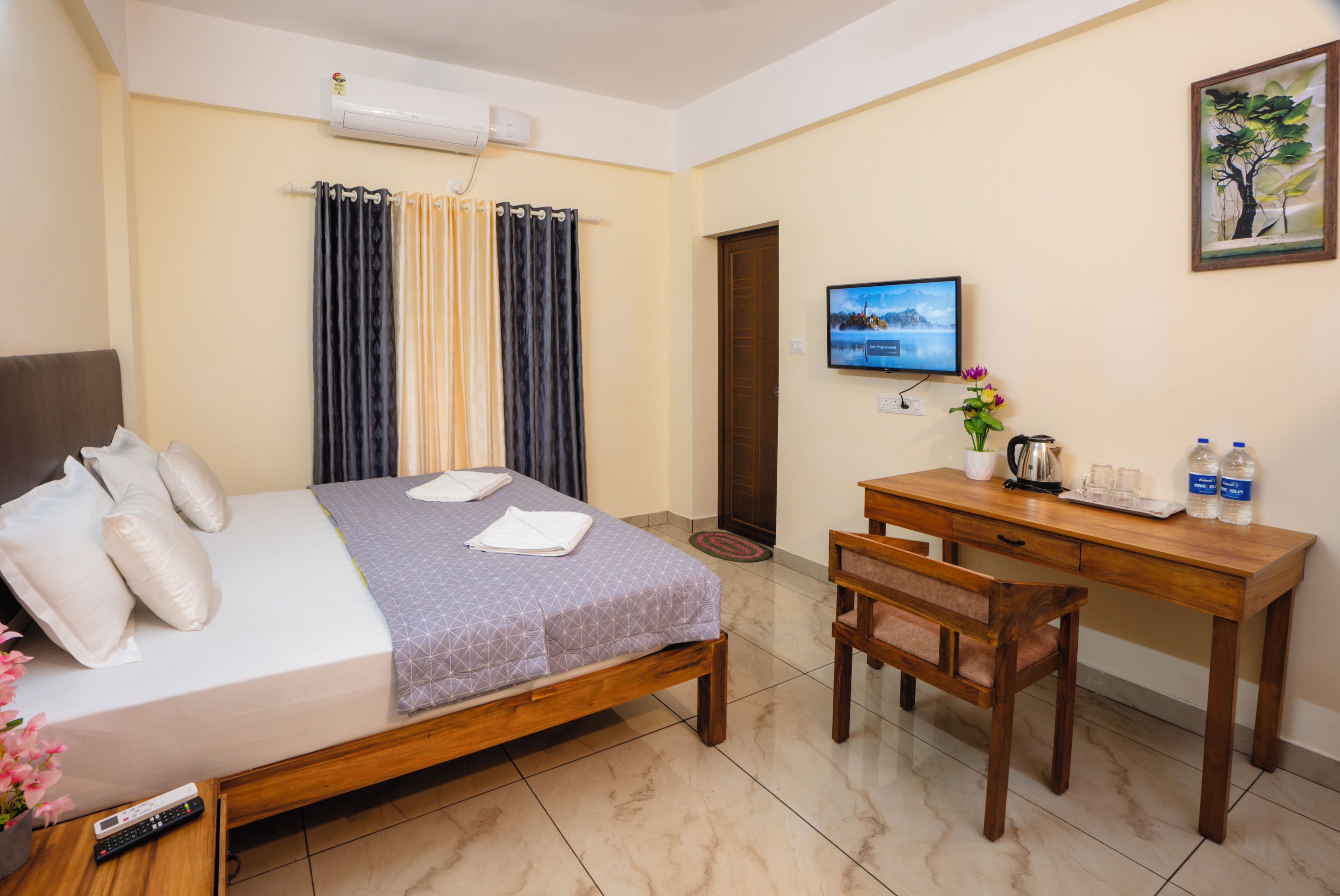 Habitación de hotel con cama, escritorio, silla, televisor y ventana con cortinas.