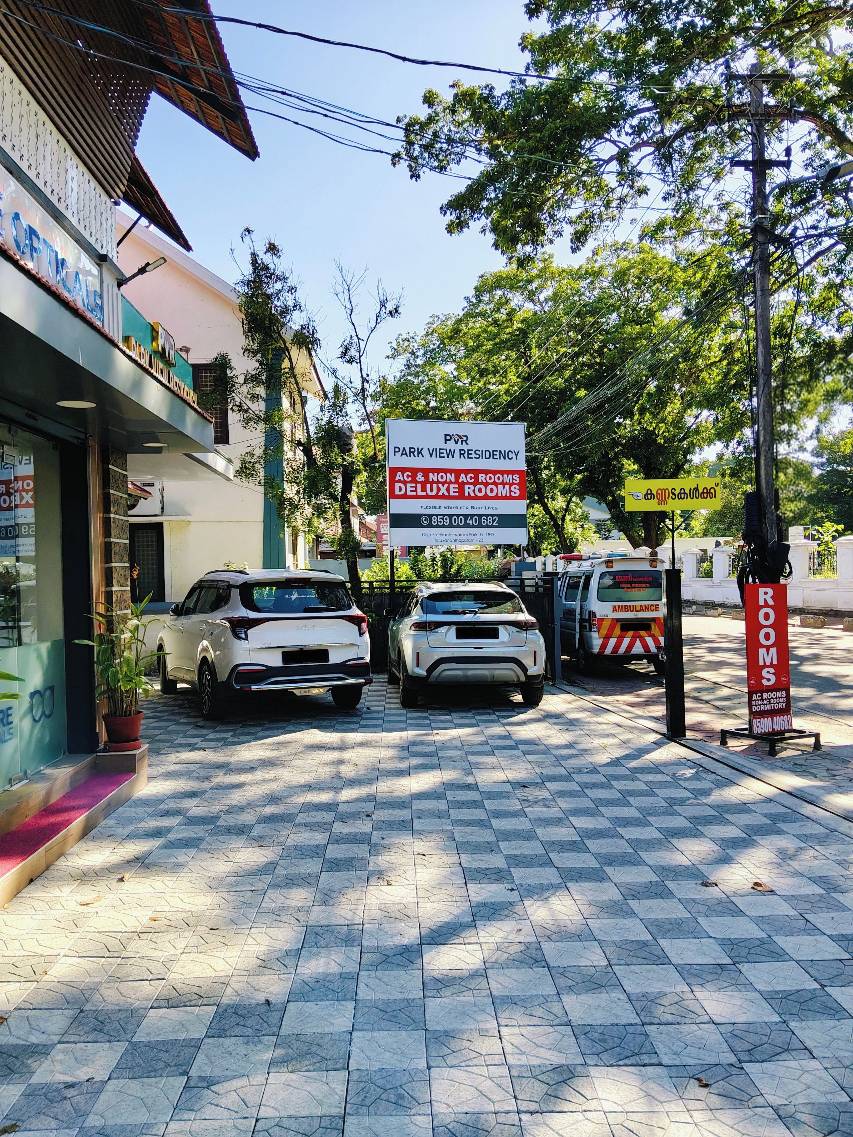 Un área de estacionamiento con un letrero que indica Park View Residency, especificando habitaciones con aire acondicionado y sin aire acondicionado, y un número de contacto.