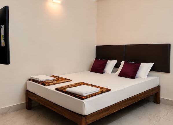 Una cama bien hecha con estructura de madera, ropa de cama blanca y dos almohadas decorativas.