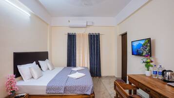 A hotel room with a bed, a desk, a television, and a window with curtains.