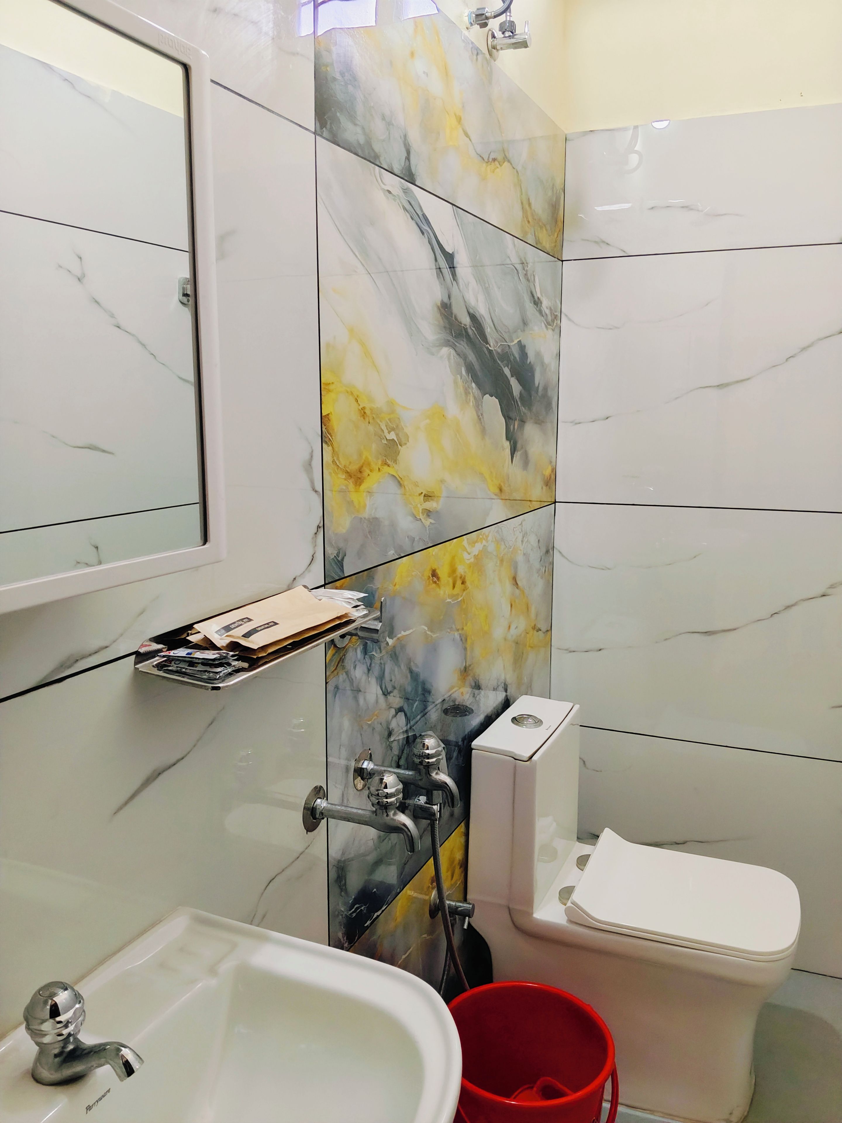 A bathroom with a sink, mirror, toilet, and a red bucket.