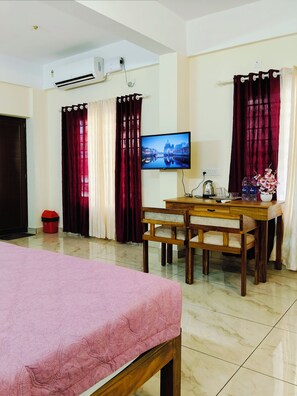 A hotel room with a bed, a desk with a chair, a television, and curtains.