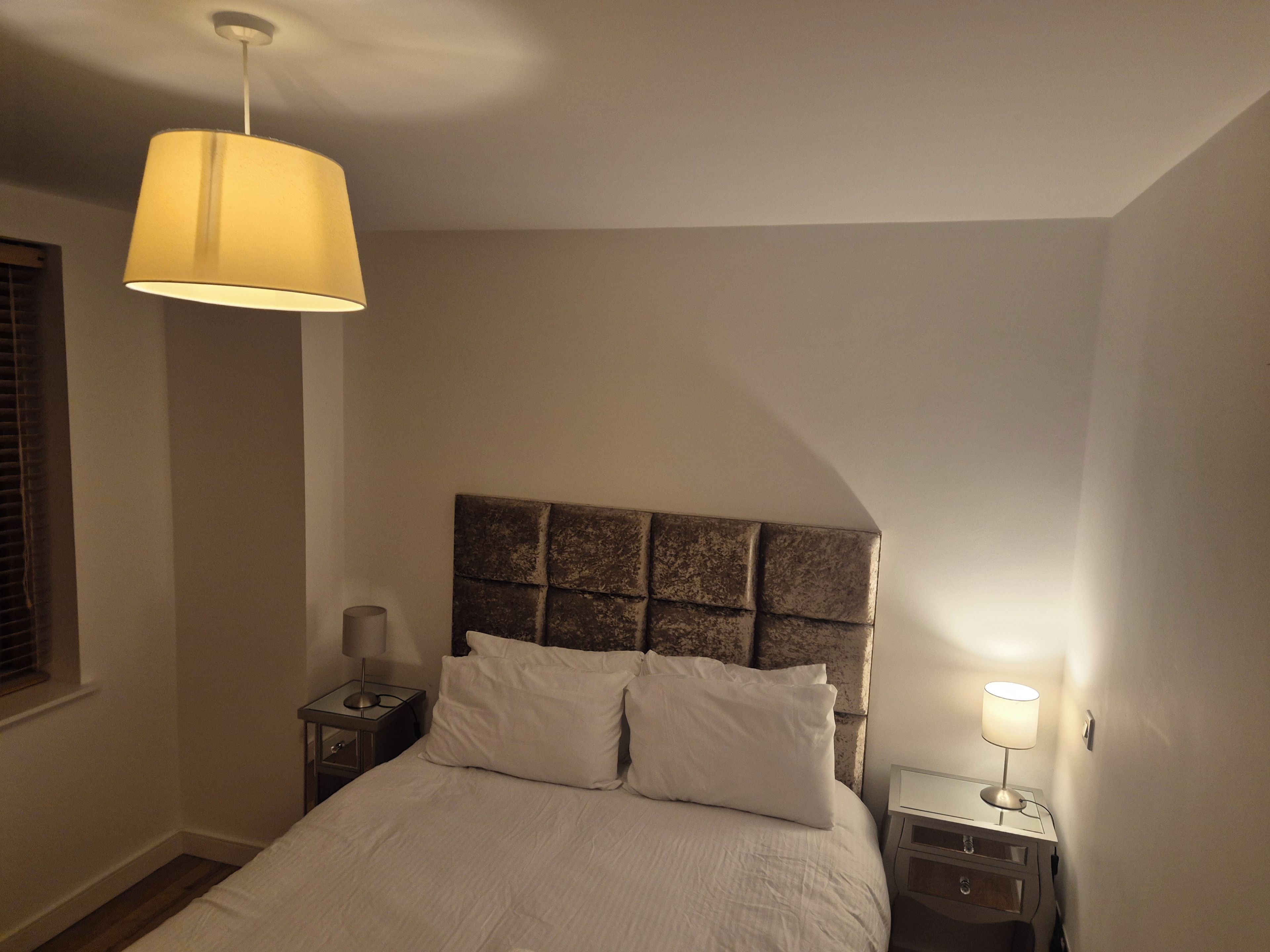Un dormitorio con una cama, dos mesitas de noche, una lámpara y un aplique colgante.