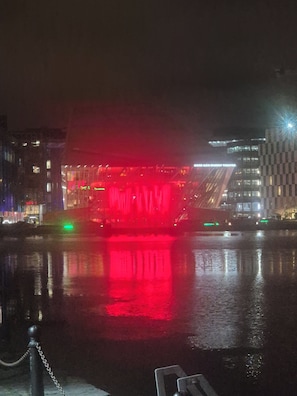 A nighttime view of a building with a red-lit facade reflecting on the water.